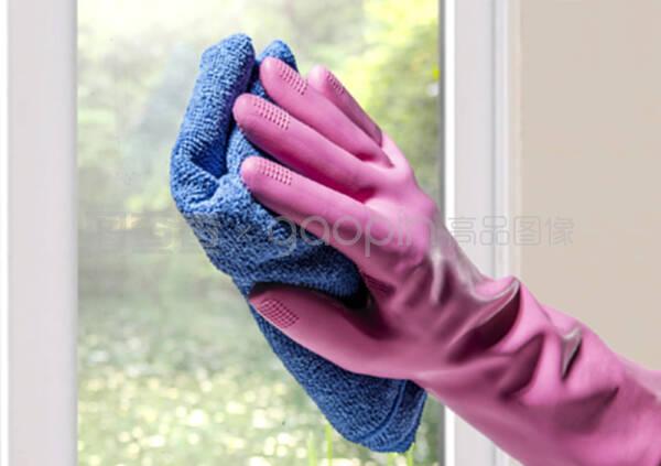 手放在橡胶手套和微纤维布擦窗玻璃上